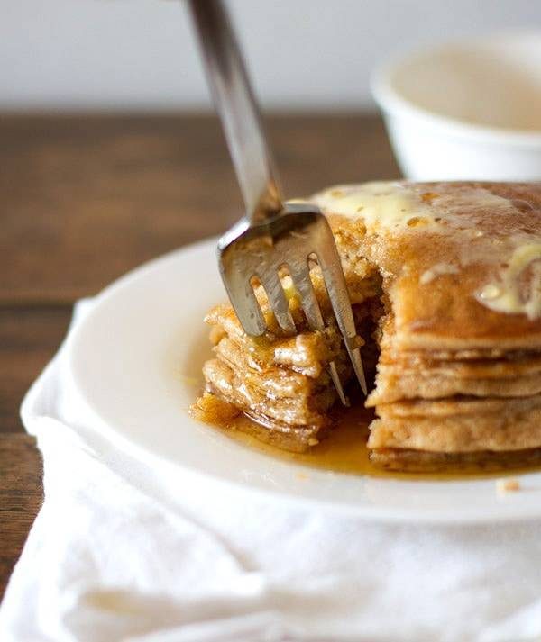 Whole wheat pancakes stacked on a plate with a fork removing a bite.