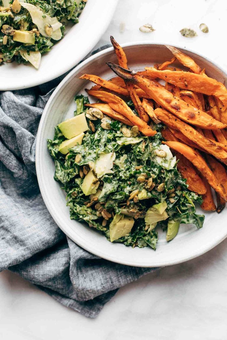 Kale caesar salad on a plate with sweet potato fries.