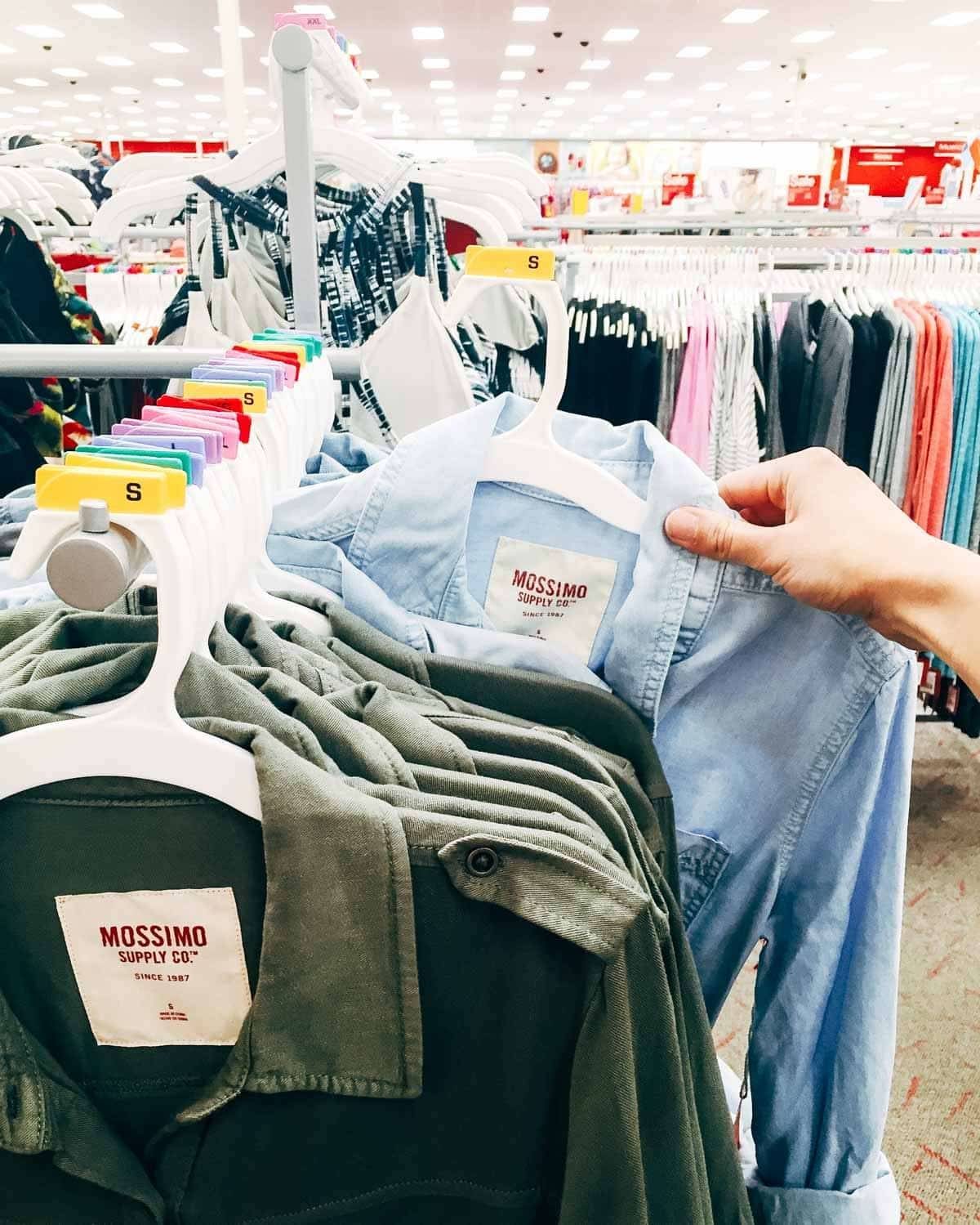 Hand pulling a shirt off of a clothing rack.